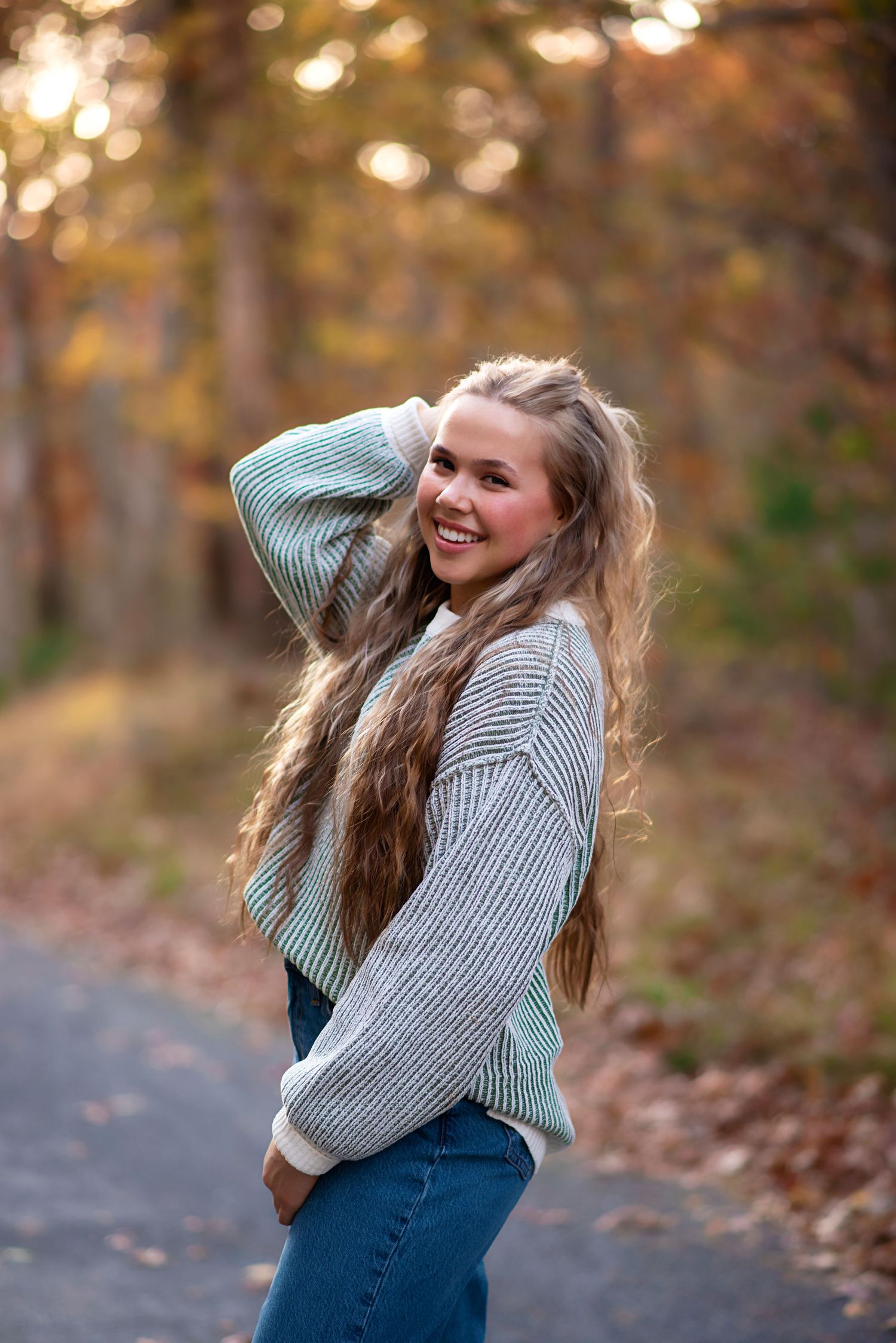 A joyful portrait of someone wearing a cozy gray sweater and jeans on an autumn path with bokeh lighting effects. Rhode Island Photographer