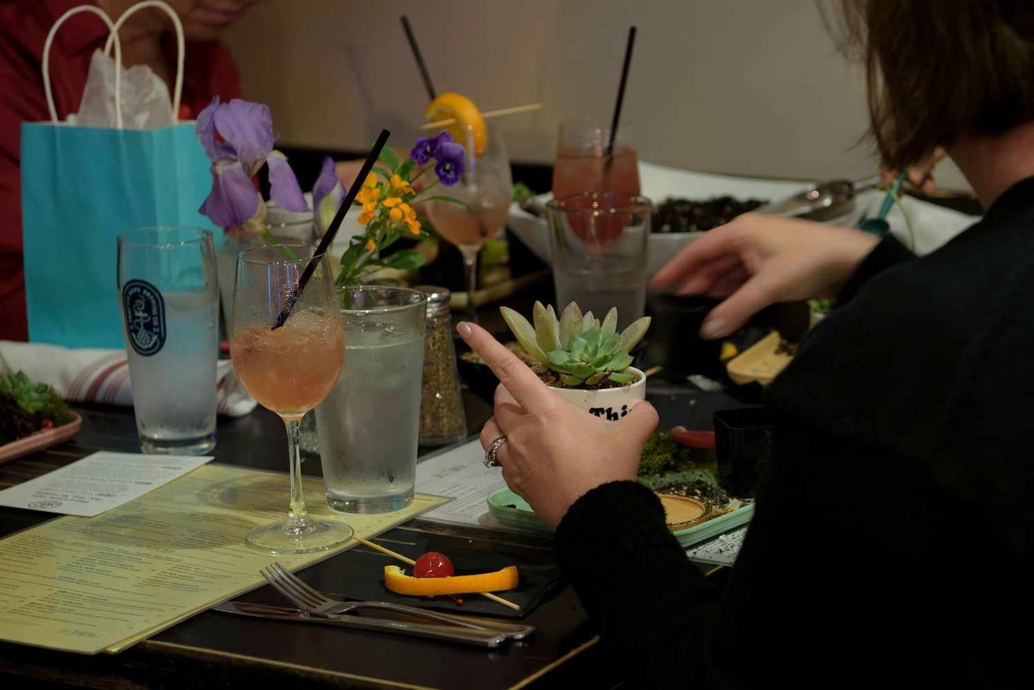 People sit at a restaurant table with colorful cocktails and dining plates in a dimly lit setting.
