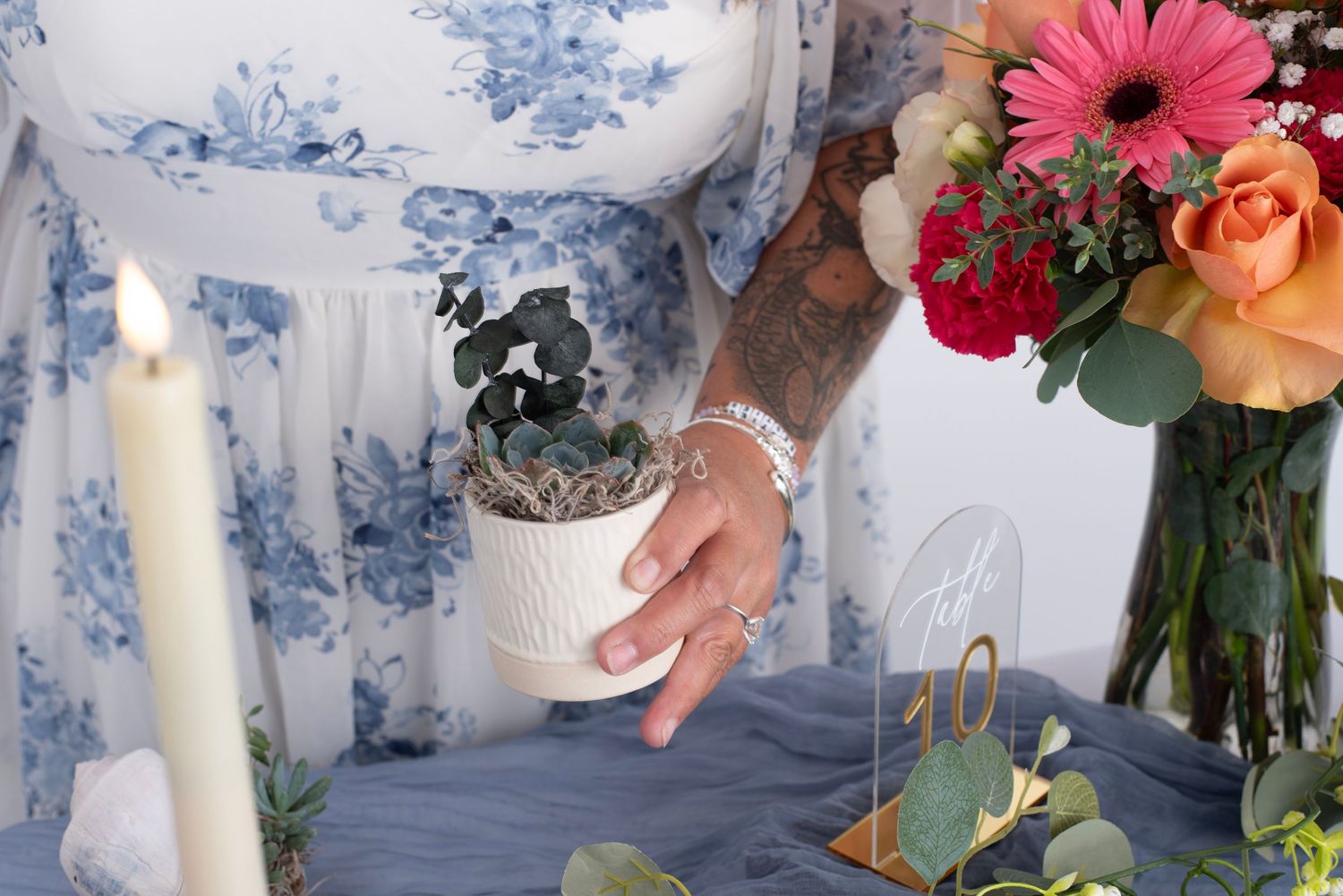 A wedding scene with white candles, floral bouquets and decorative elements against a textured blue backdrop.