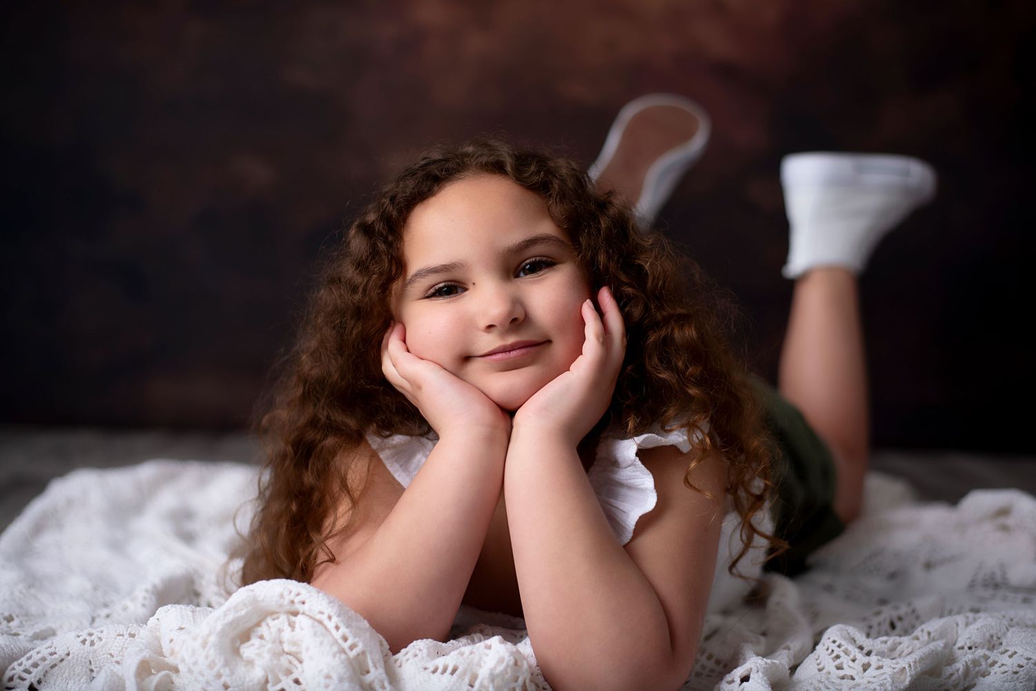 Young child with curly hair laying on white bedding in black and white tones with dramatic lighting effect.