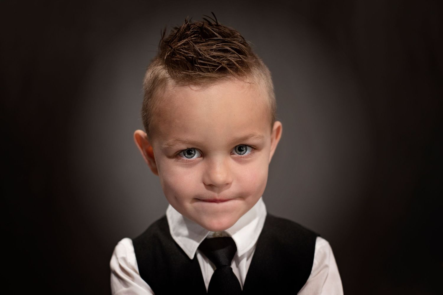 A series of black and white portraits showing a young child in formal attire against a dark background.