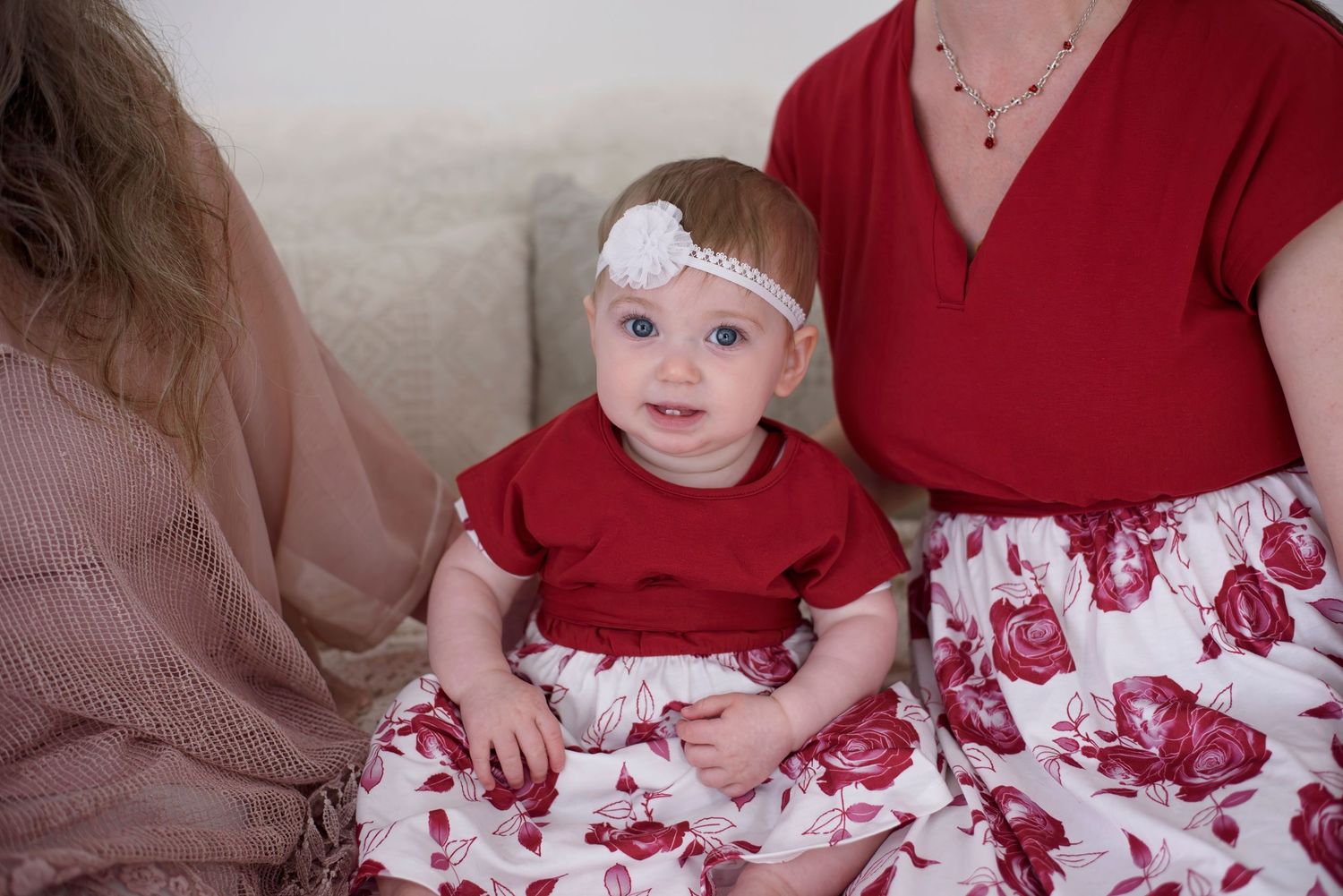 Small child in matching red and white floral outfit sits on couch between two adults wearing coordinating outfits.