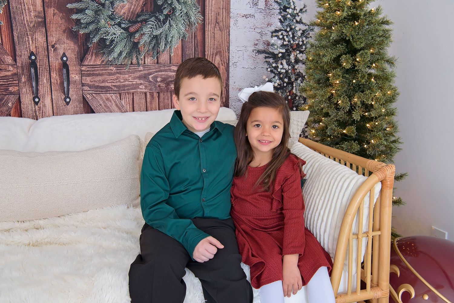 Two people in coordinating green and burgundy outfits pose together by a decorated Christmas tree.