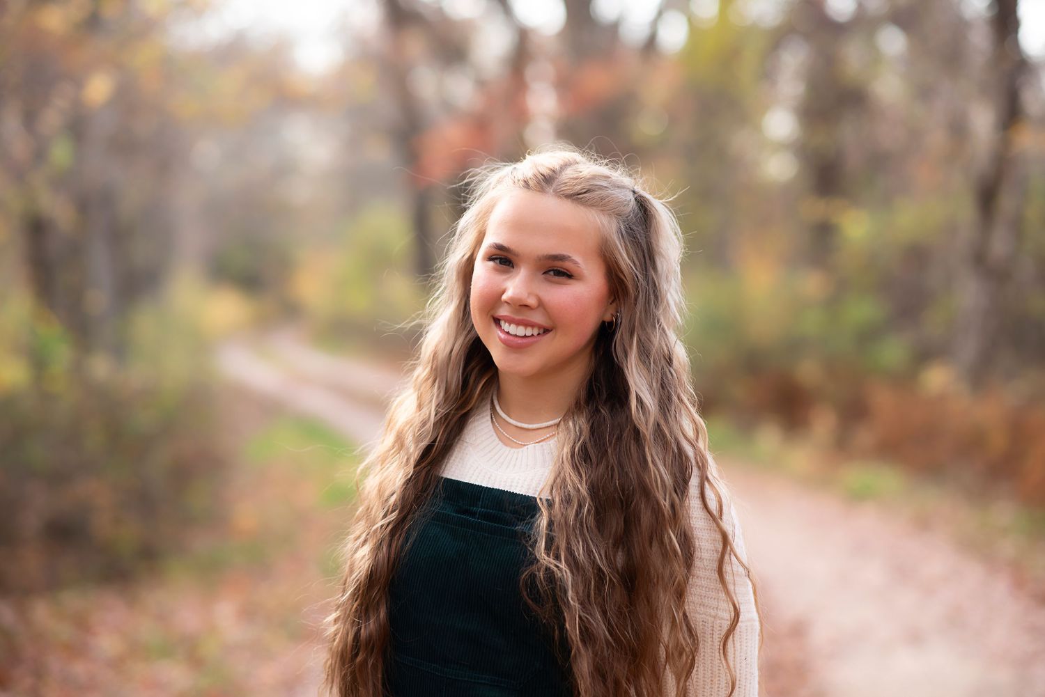 Beautiful outdoor portrait with long wavy hair wearing a dark sweater smiling in a fall setting with warm backlighting.