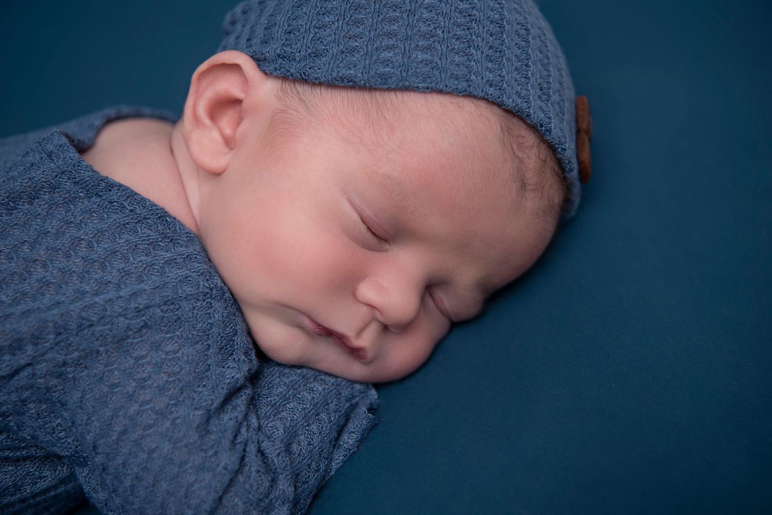 Sleeping baby wearing gray knit sweater rests peacefully in professional newborn photography session.