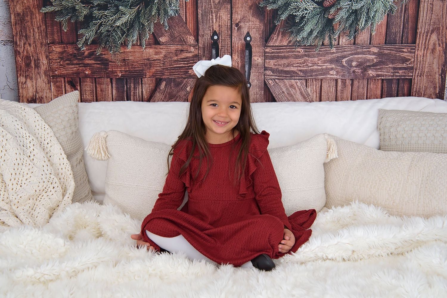 A person in a burgundy sweater sits on a white couch with festive holiday decorations in the background.