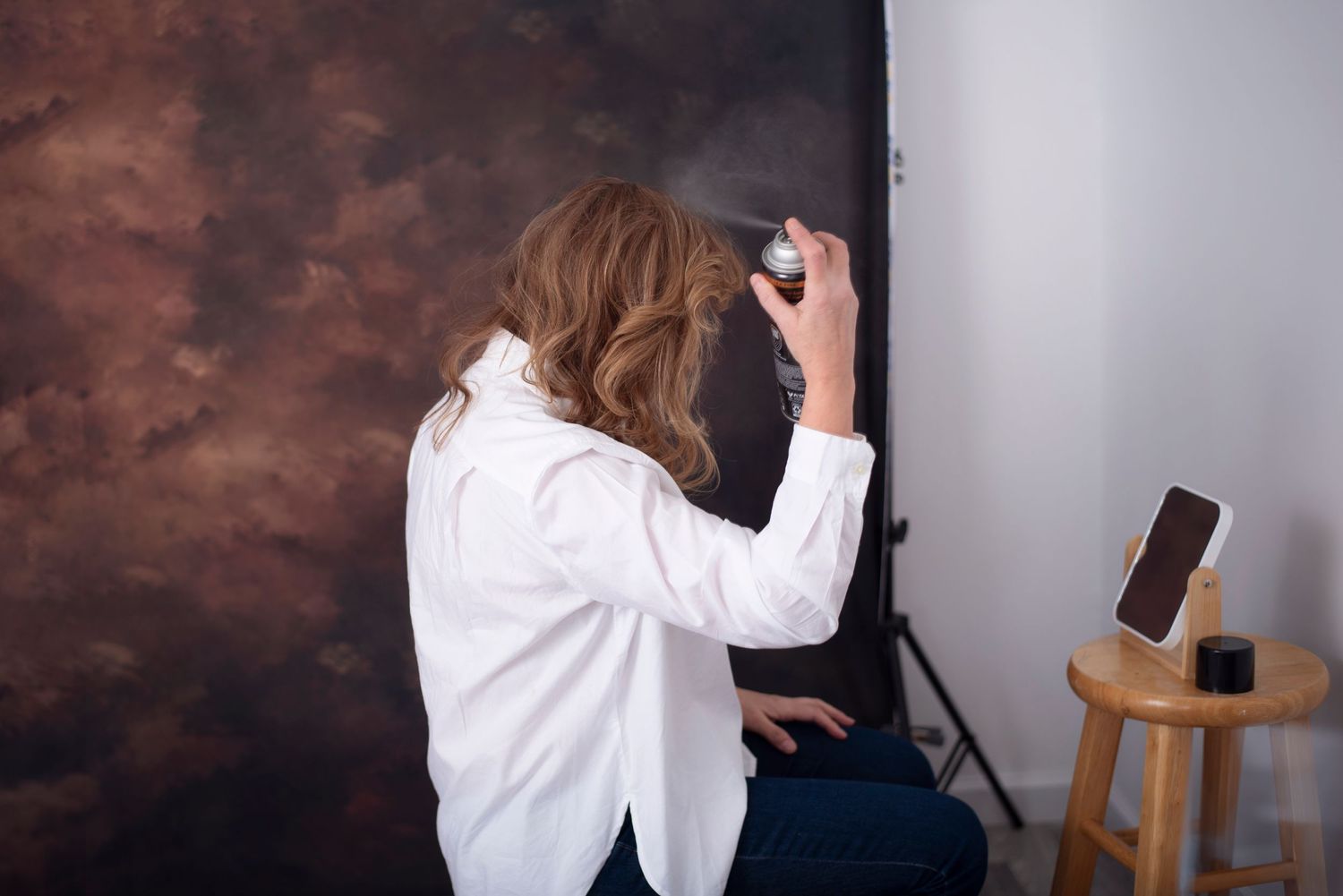 A person in a white shirt writes on a wall against a brown backdrop in a studio setting.