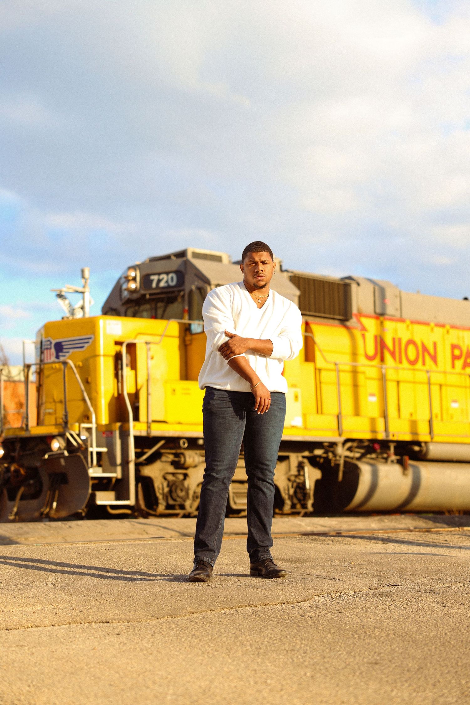 Man in white shirt and jeans stands confidently before Union Pacific train.