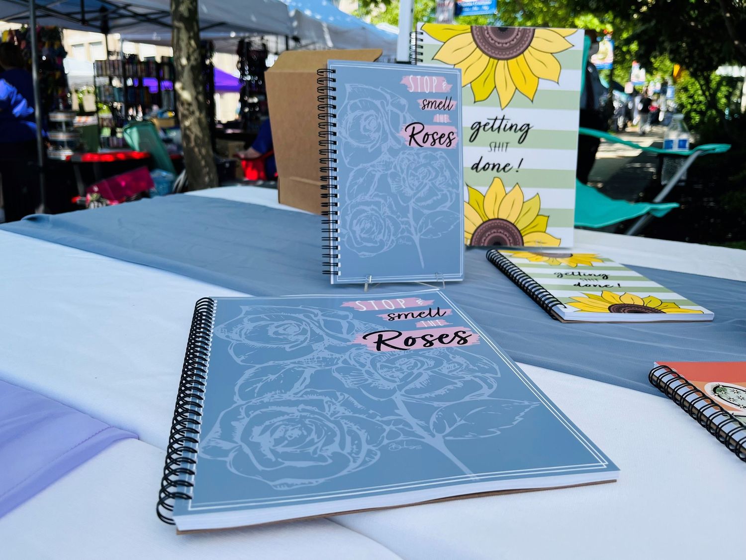 Spiral-bound notebooks with roses and sunflower designs on display at a market.