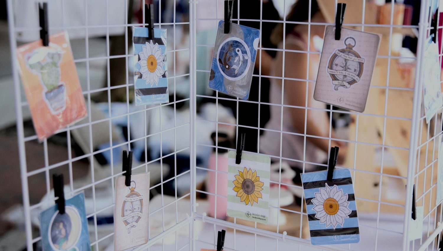 Assorted vinyl stickers with various designs, including a cactus, a daisy, a yin yang fish, and a compass, displayed on a white grid stand