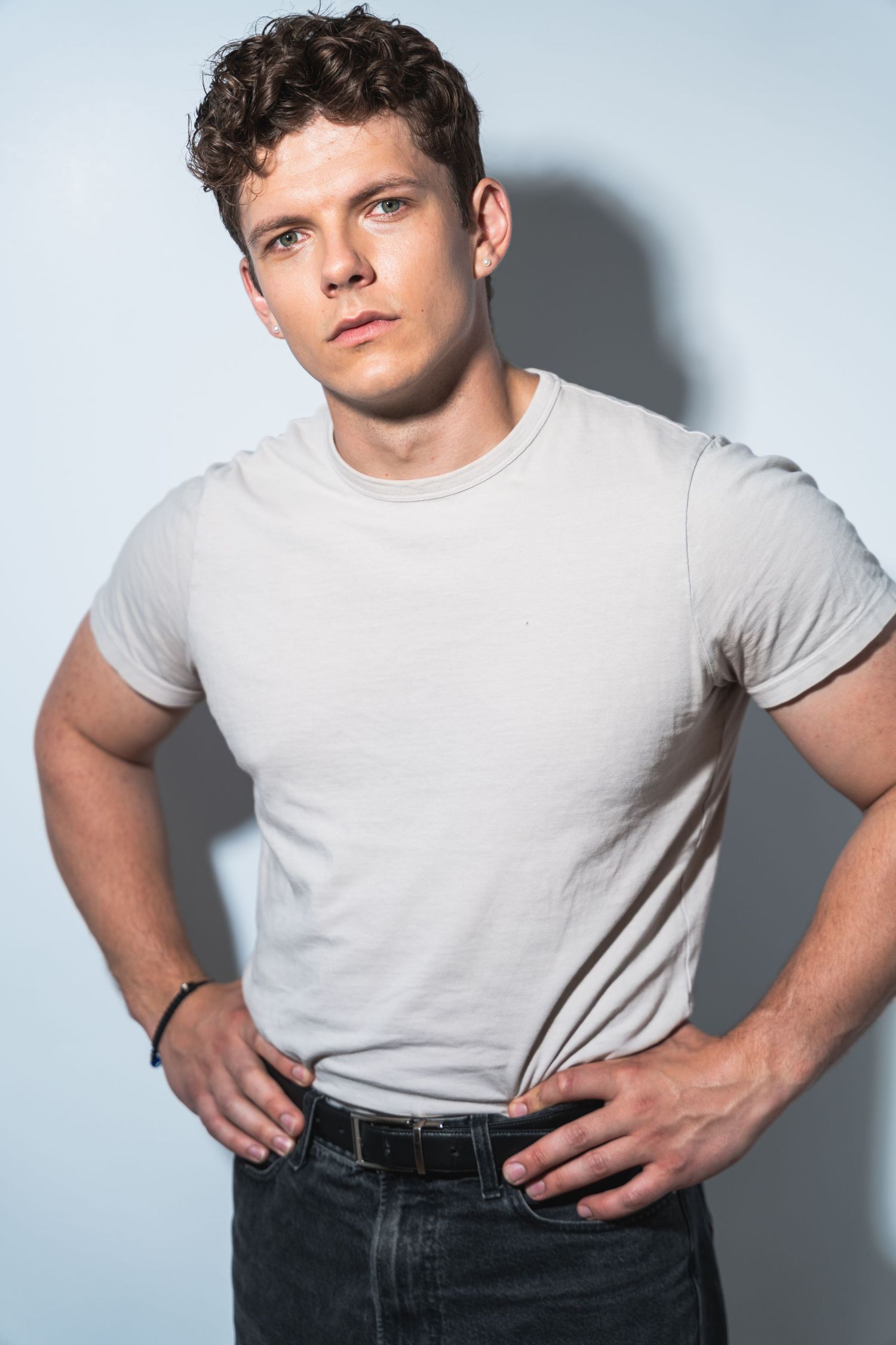 Professional studio portrait of person in white t-shirt and dark jeans against light background.