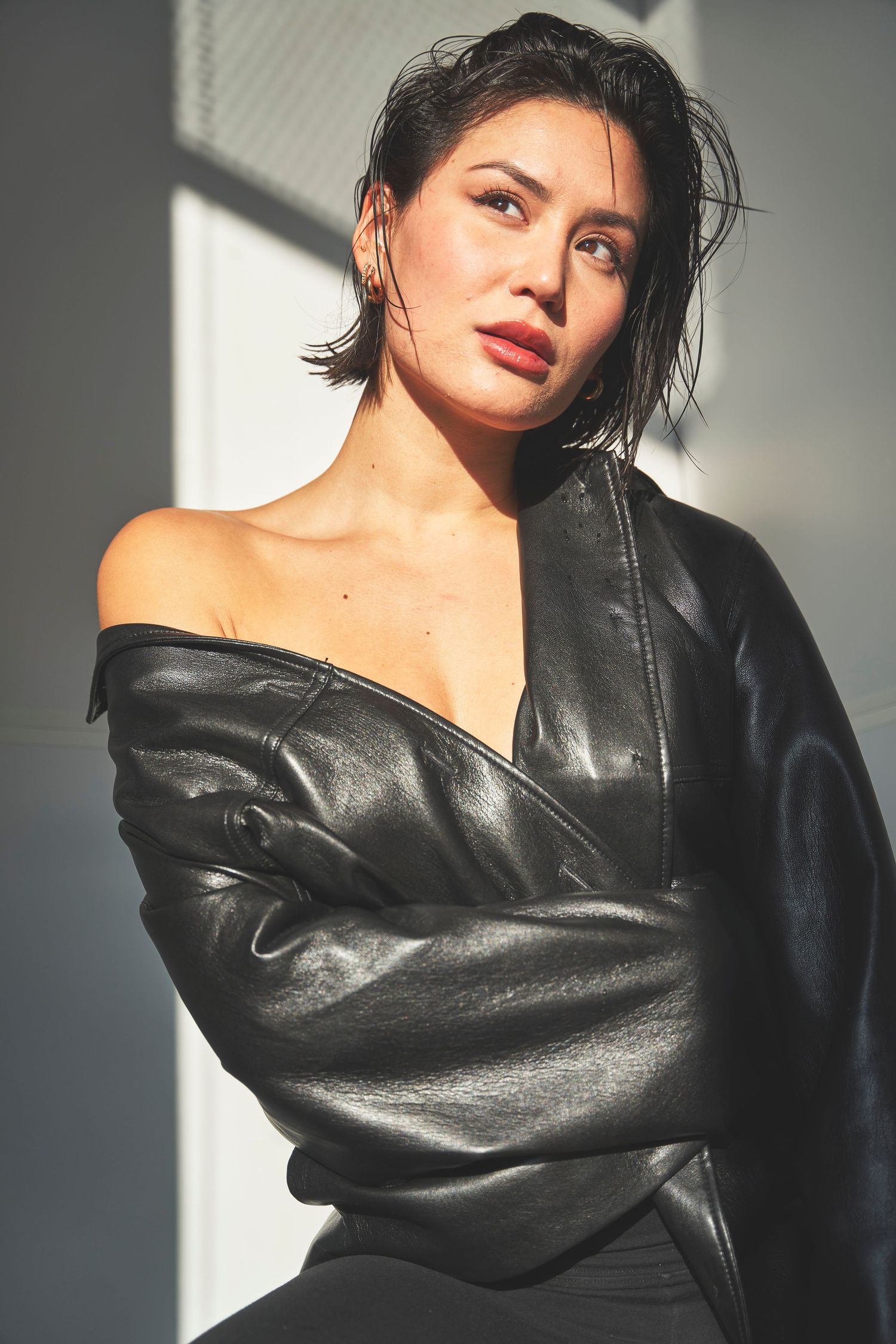 Portrait in dramatic lighting featuring a black leather jacket worn off-shoulder against a light background.