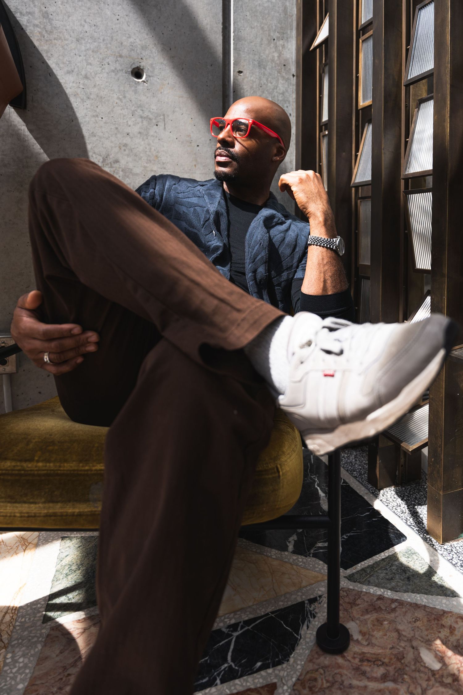 Person wearing red sunglasses and navy shirt poses casually in retro setting with geometric floor tiles.