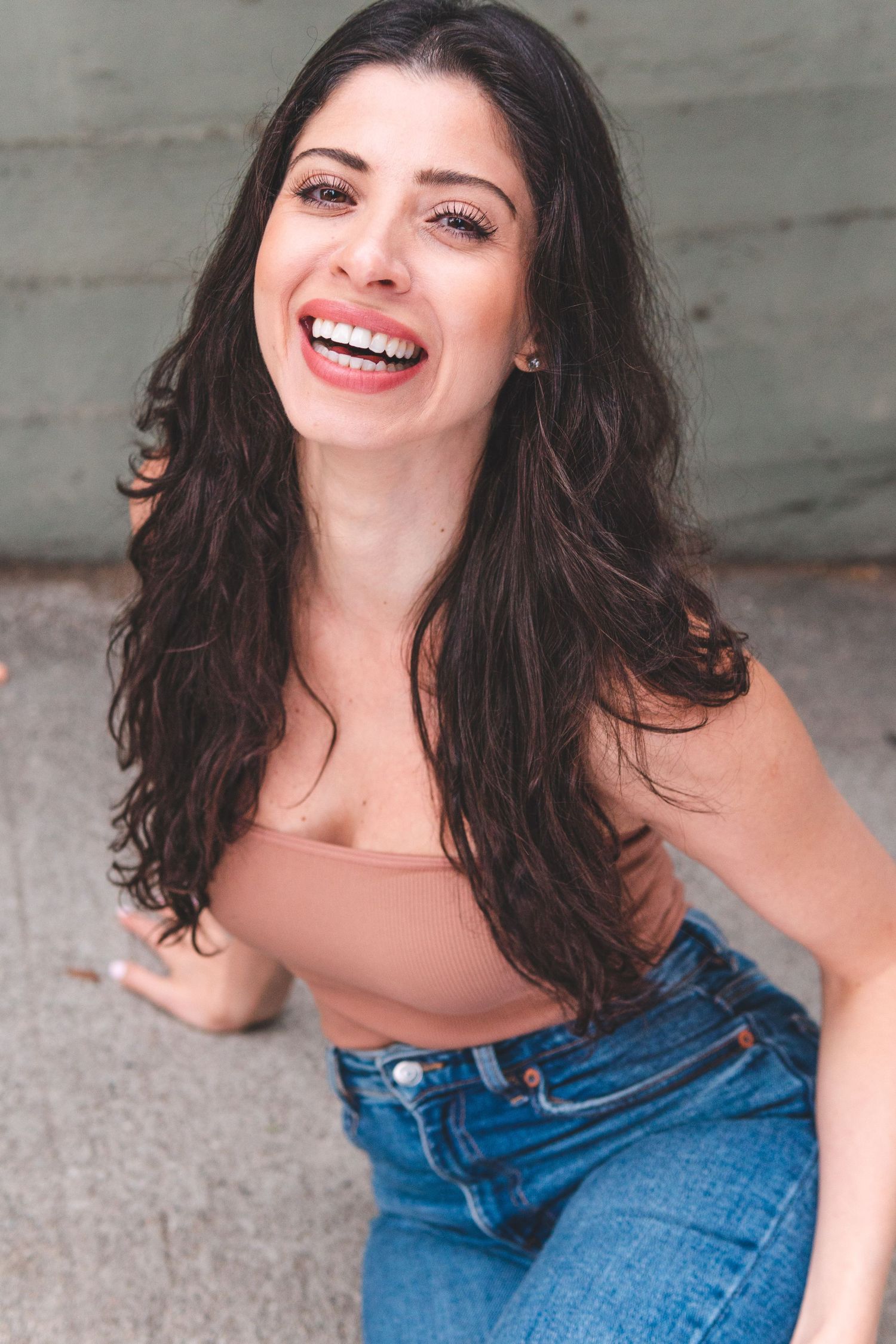 Woman with dark wavy hair laughs joyfully while wearing denim in a casual photo series.