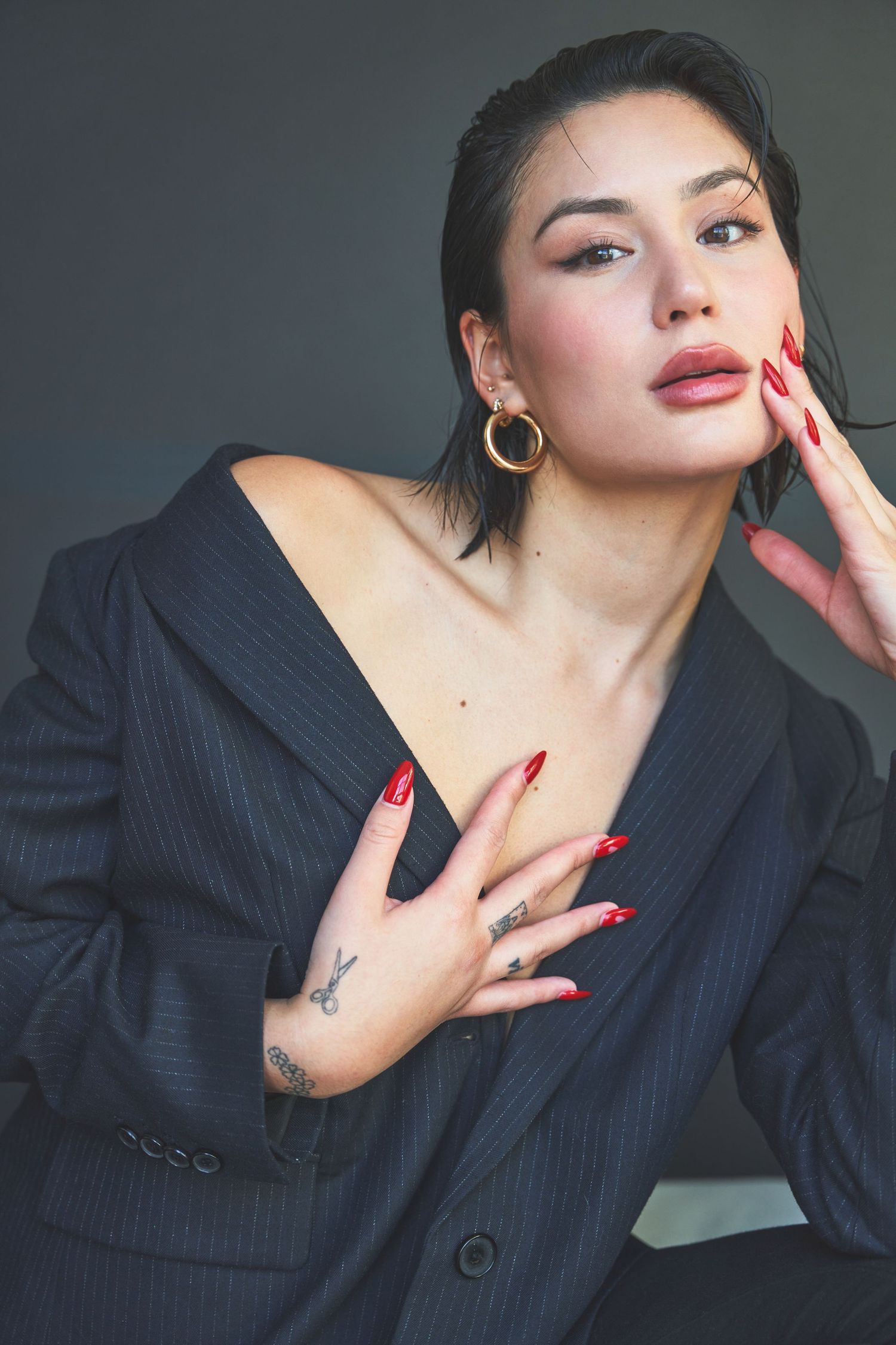 Fashion portrait featuring red nails, gold hoops and pinstriped blazer against dark background.
