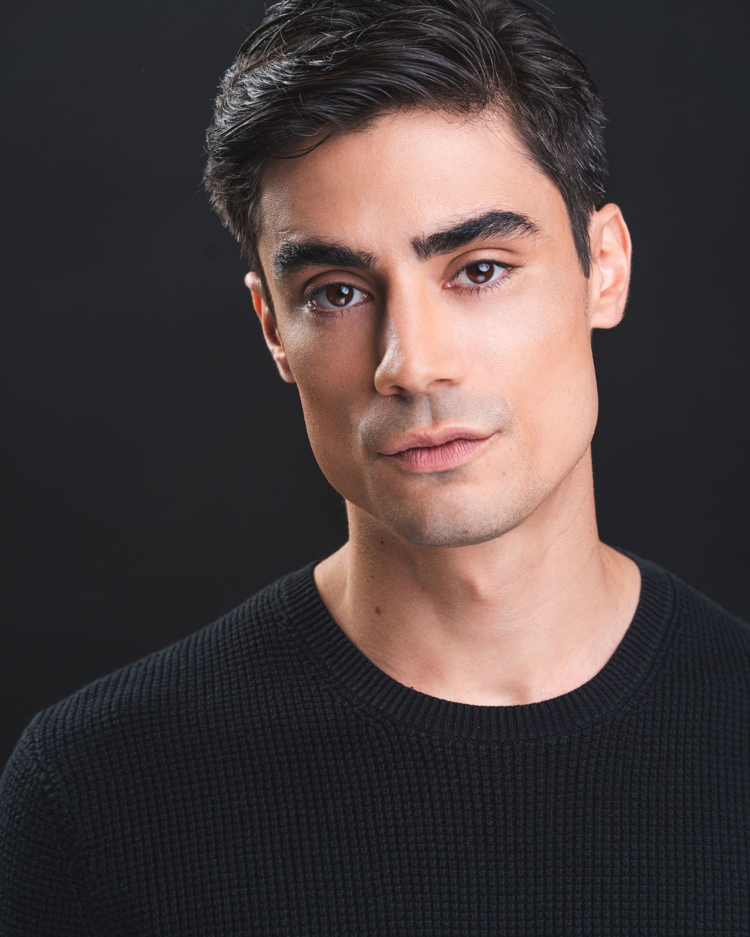 A professional headshot of a man with dark hair wearing a black sweater against a dark background.
