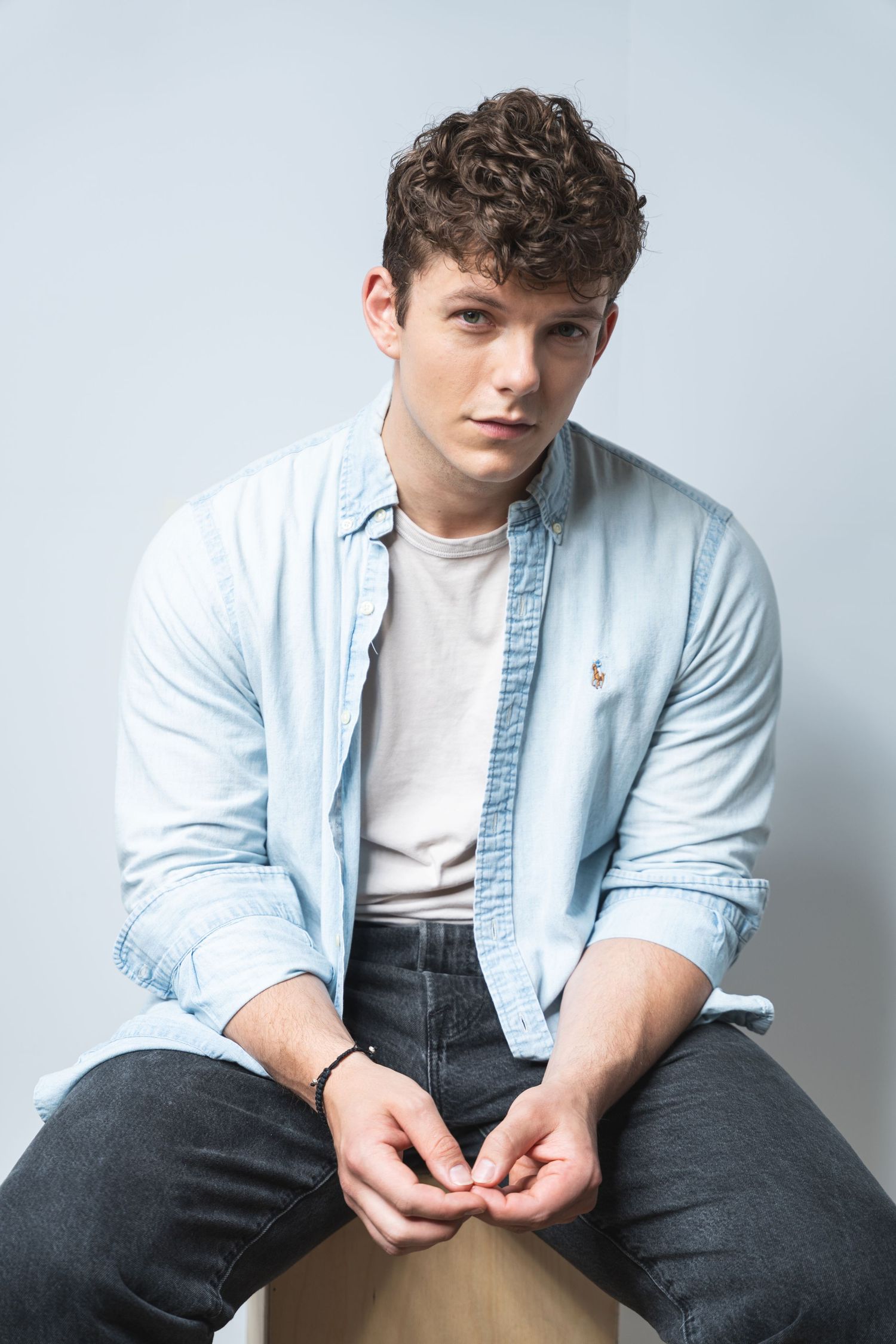 Portrait in casual attire featuring light denim button-down shirt and white t-shirt against neutral background.