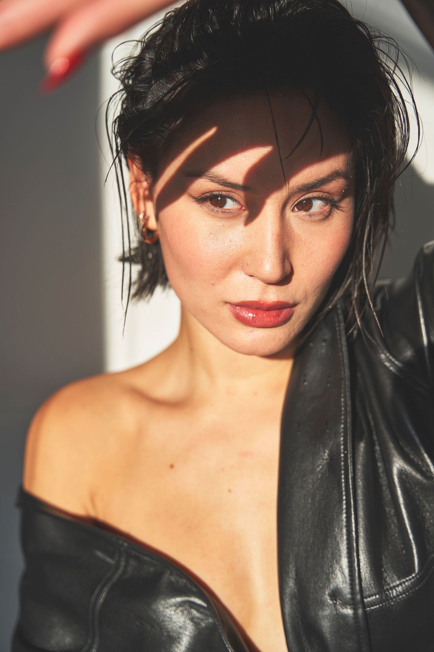 Portrait of a model wearing a black leather jacket in dramatic lighting with red lipstick and dark hair styled up.