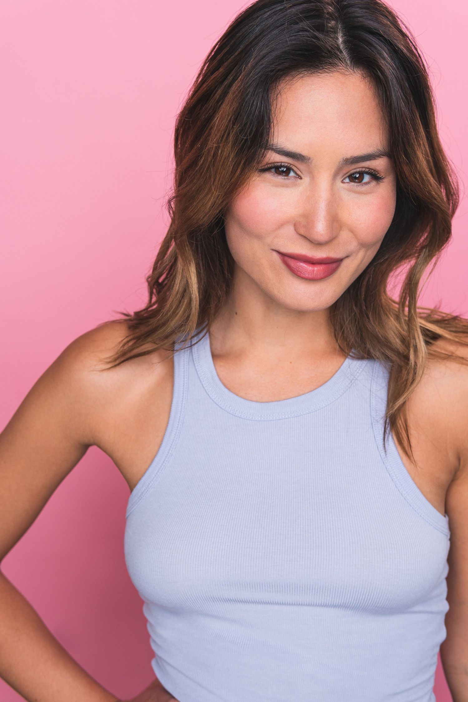 Professional headshot against pink background showing warm smile and wearing a light blue sleeveless top.