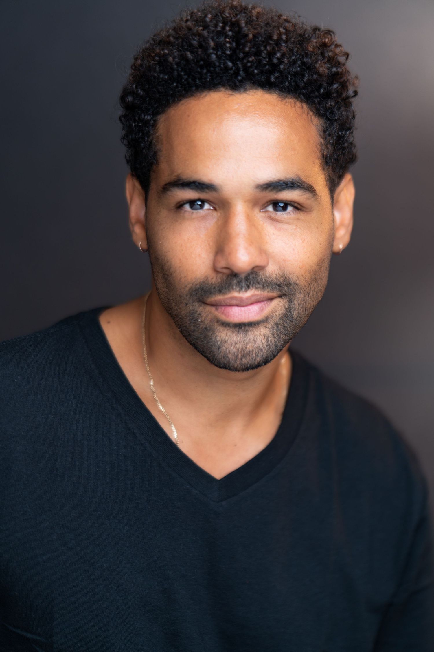 Professional studio portrait against dark background wearing a black v-neck shirt.