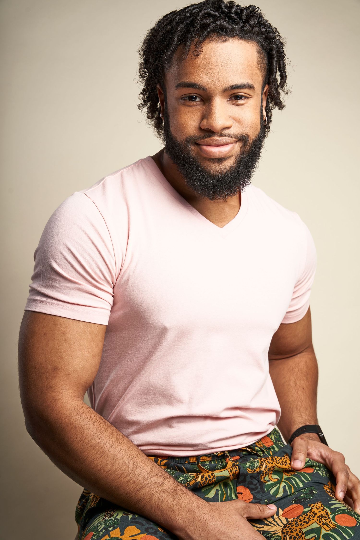 Smiling person in pink t-shirt and patterned pants sits casually in series of cropped portraits against neutral background.