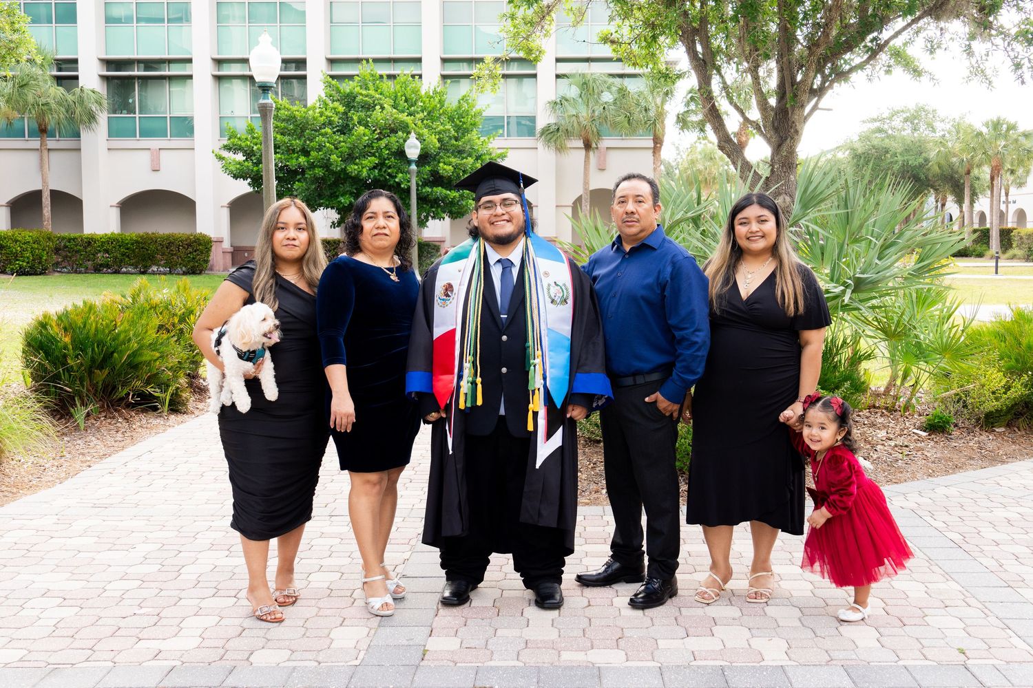 Family celebrating a college graduation outdoors, graduate in cap and gown with colorful stoles. Florida Gulf Coast University Graduation.