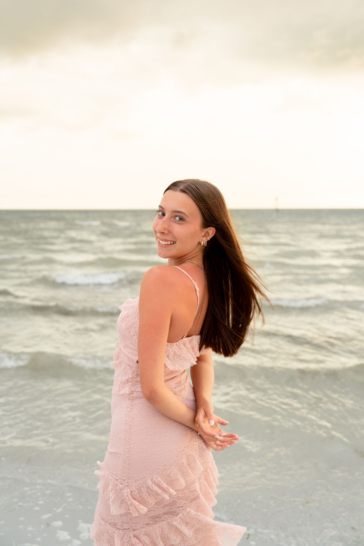 Young woman in pink dress smiling on beach at sunset with ocean waves behind her. Fort Myers Beach, Florida