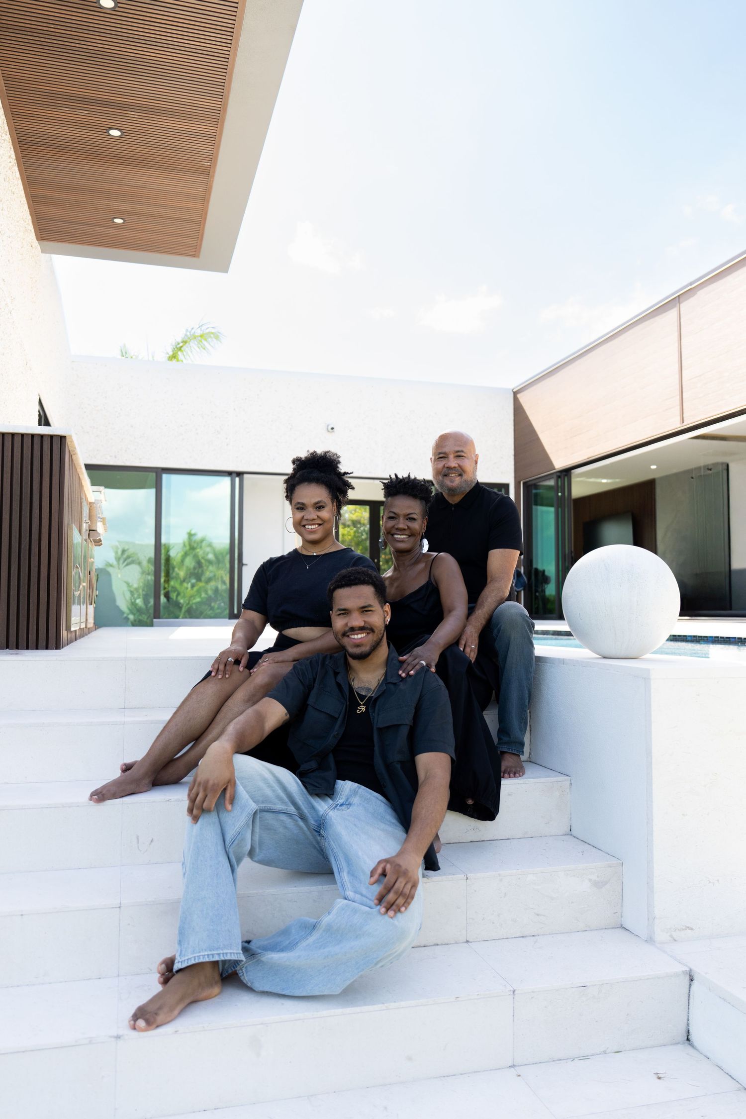 Family of four in black outfits posing on white marble steps of a contemporary home.