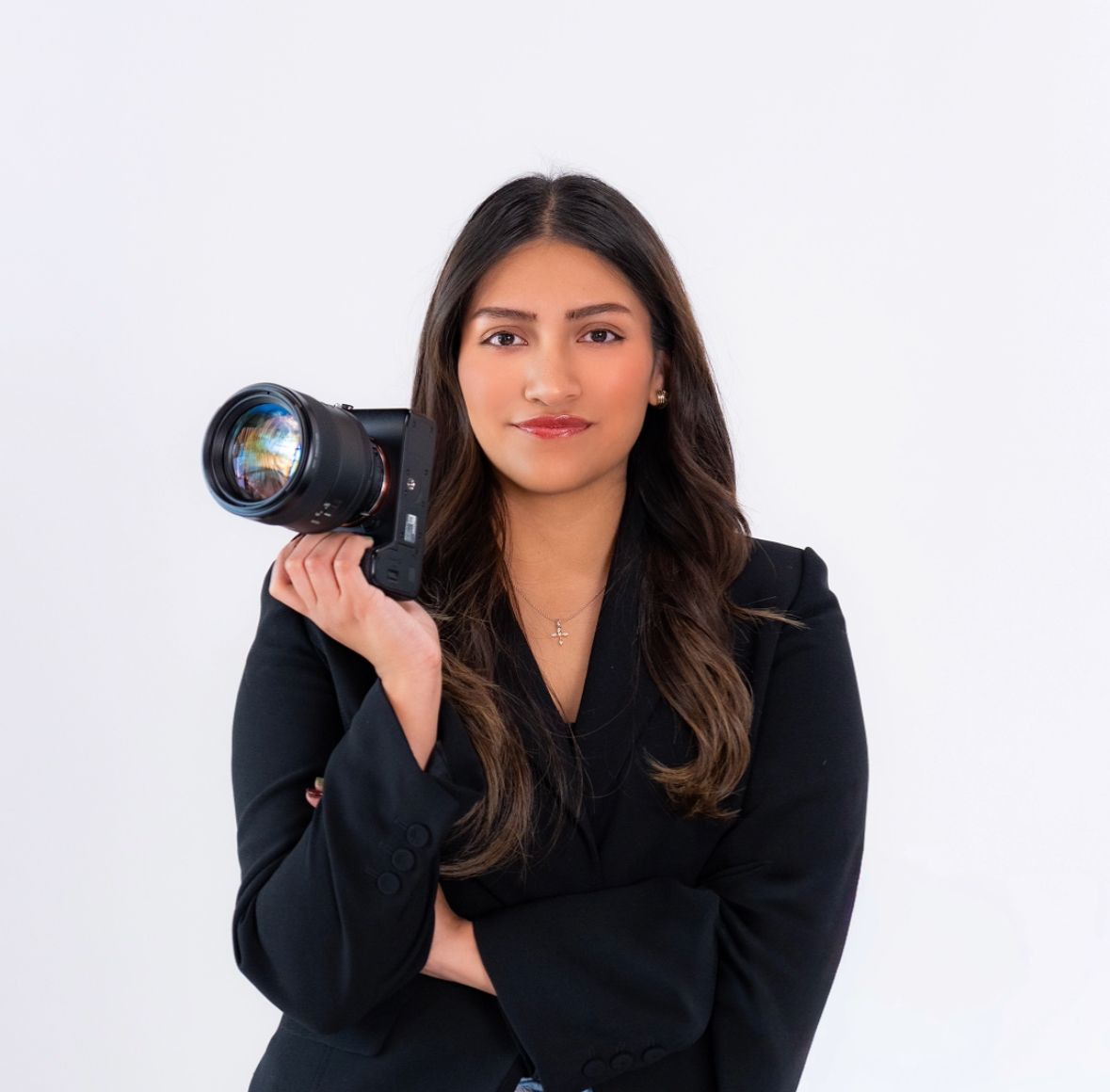 Confident female photographer holding camera in black blazer against white background.