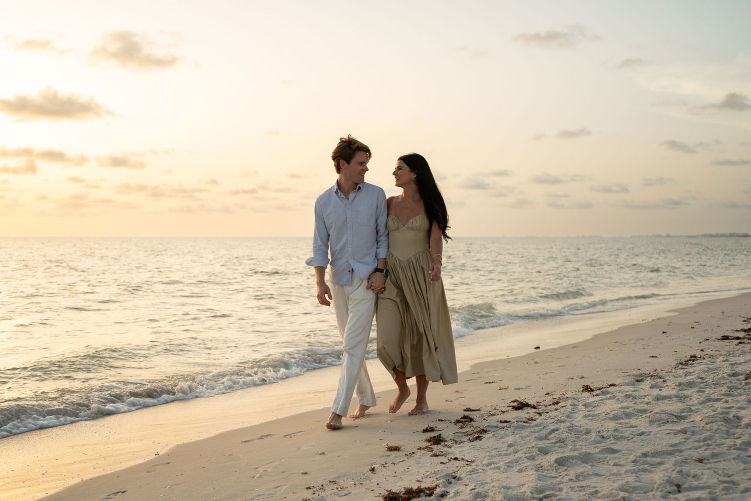 Couple walking hand in hand along a white sandy beach at golden sunset hour.