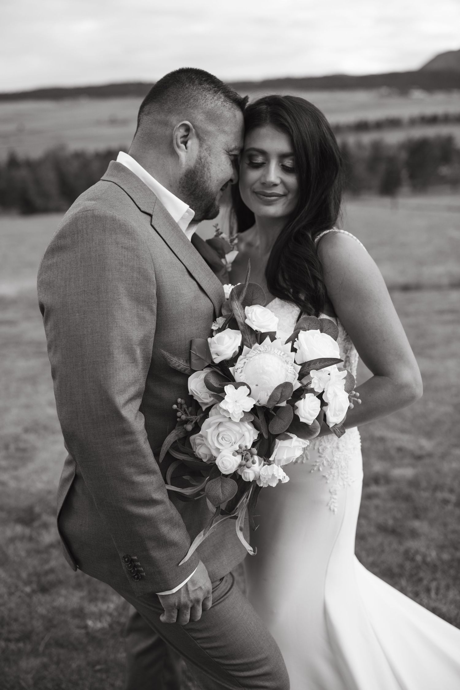 Black and white wedding portrait of a couple sharing an intimate moment outdoors with a beautiful bouquet of white roses.