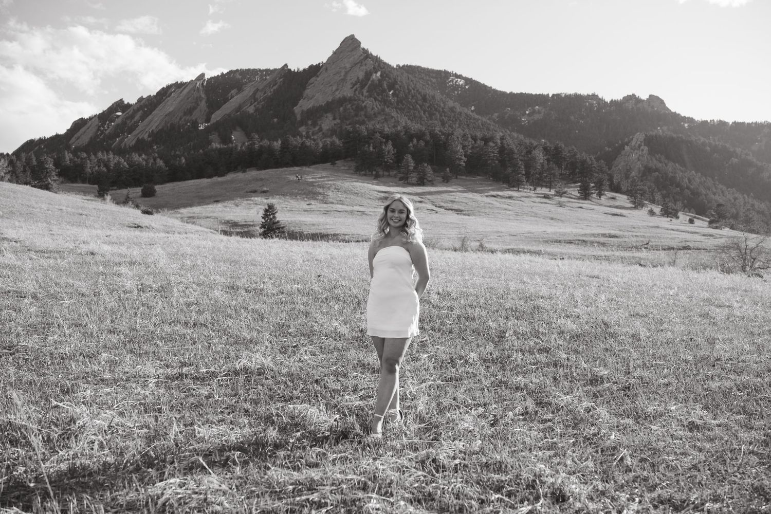 Black and white photo of person standing in field with mountain peak in background.