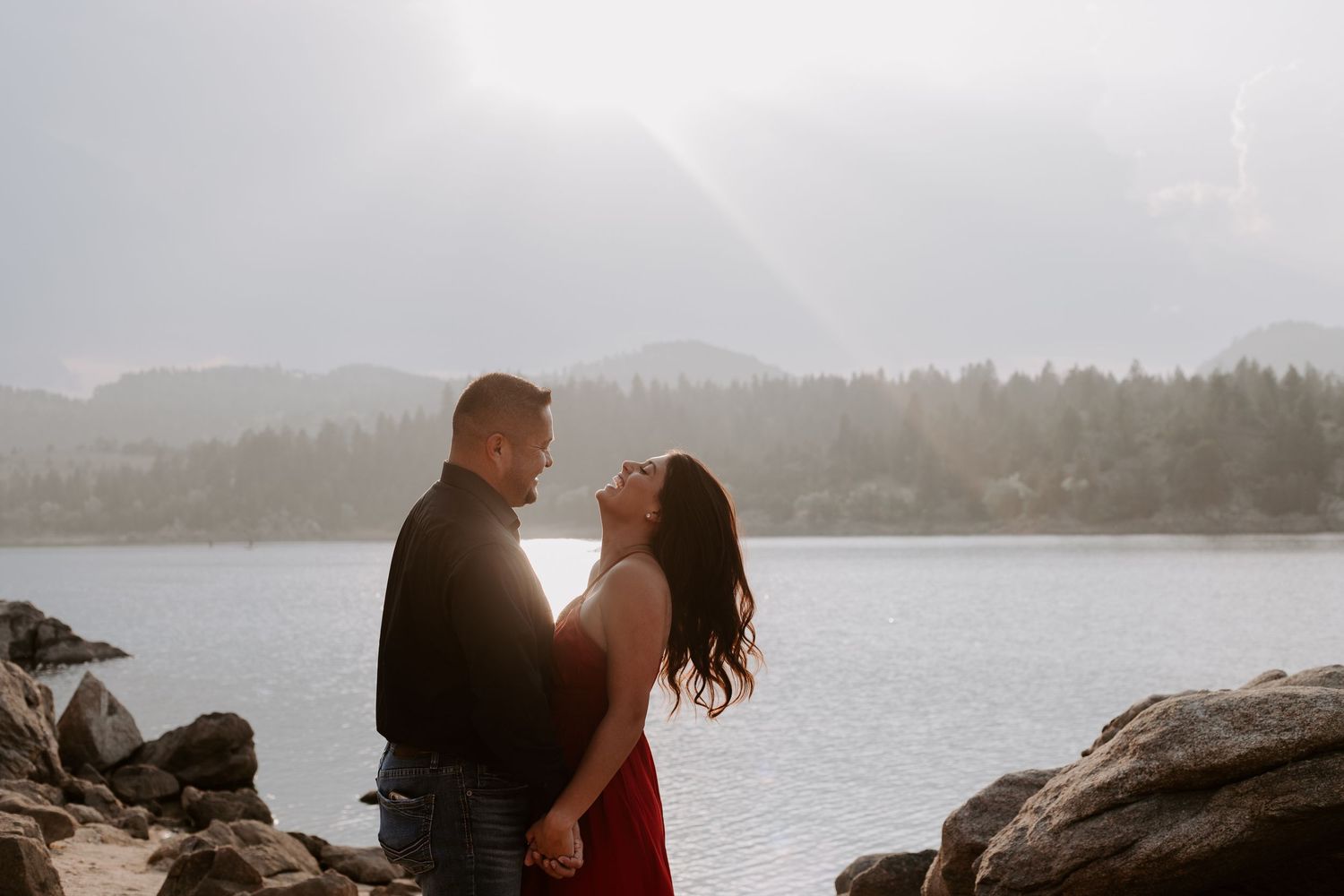 A silhouetted couple shares a romantic moment against a misty lake and mountain backdrop.