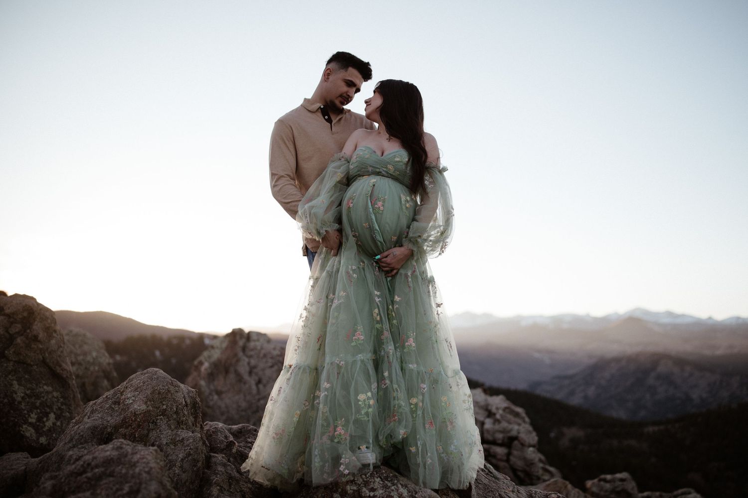 Romantic mountain-top maternity portrait with couple in elegant attire at dusk.