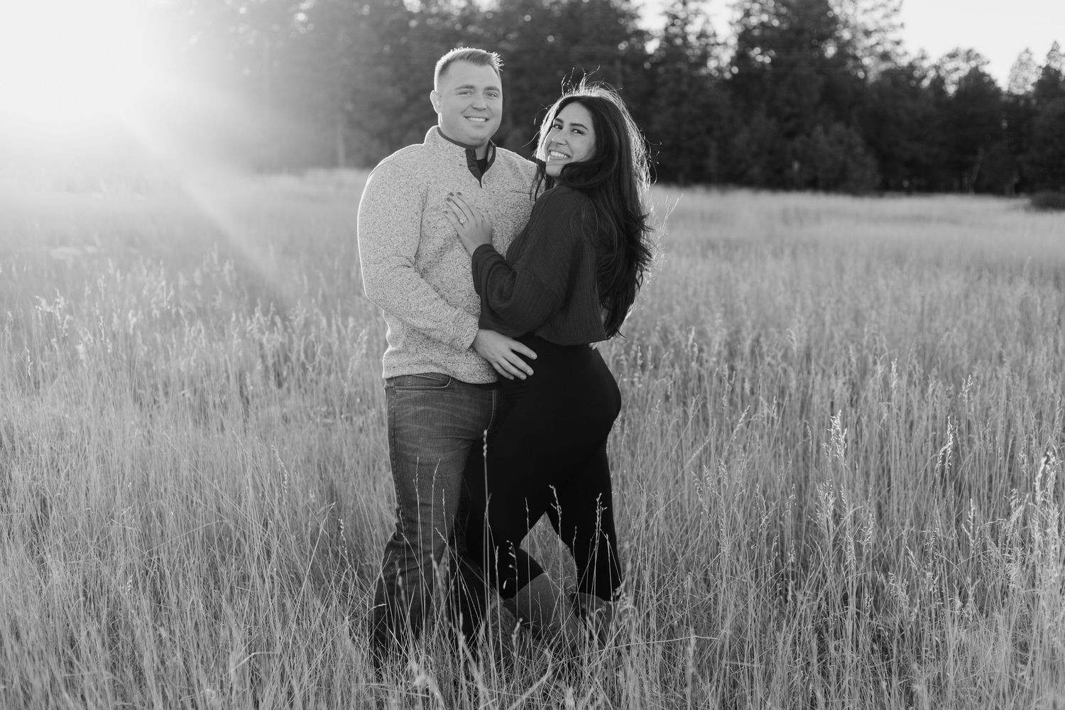 A couple embracing in a sunlit field with tall grass during a romantic photoshoot.