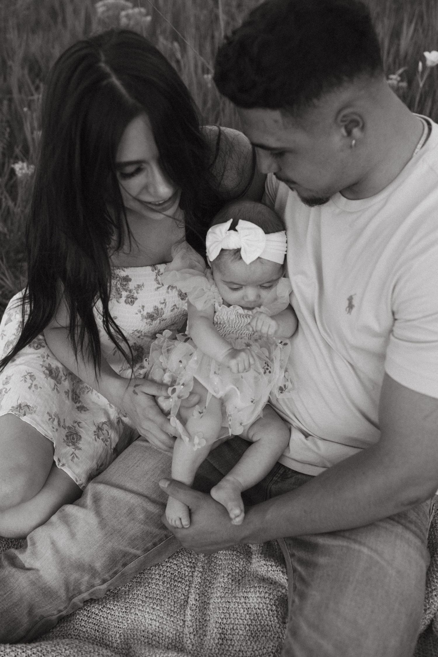 Black and white intimate family portrait on picnic blanket in grass field.