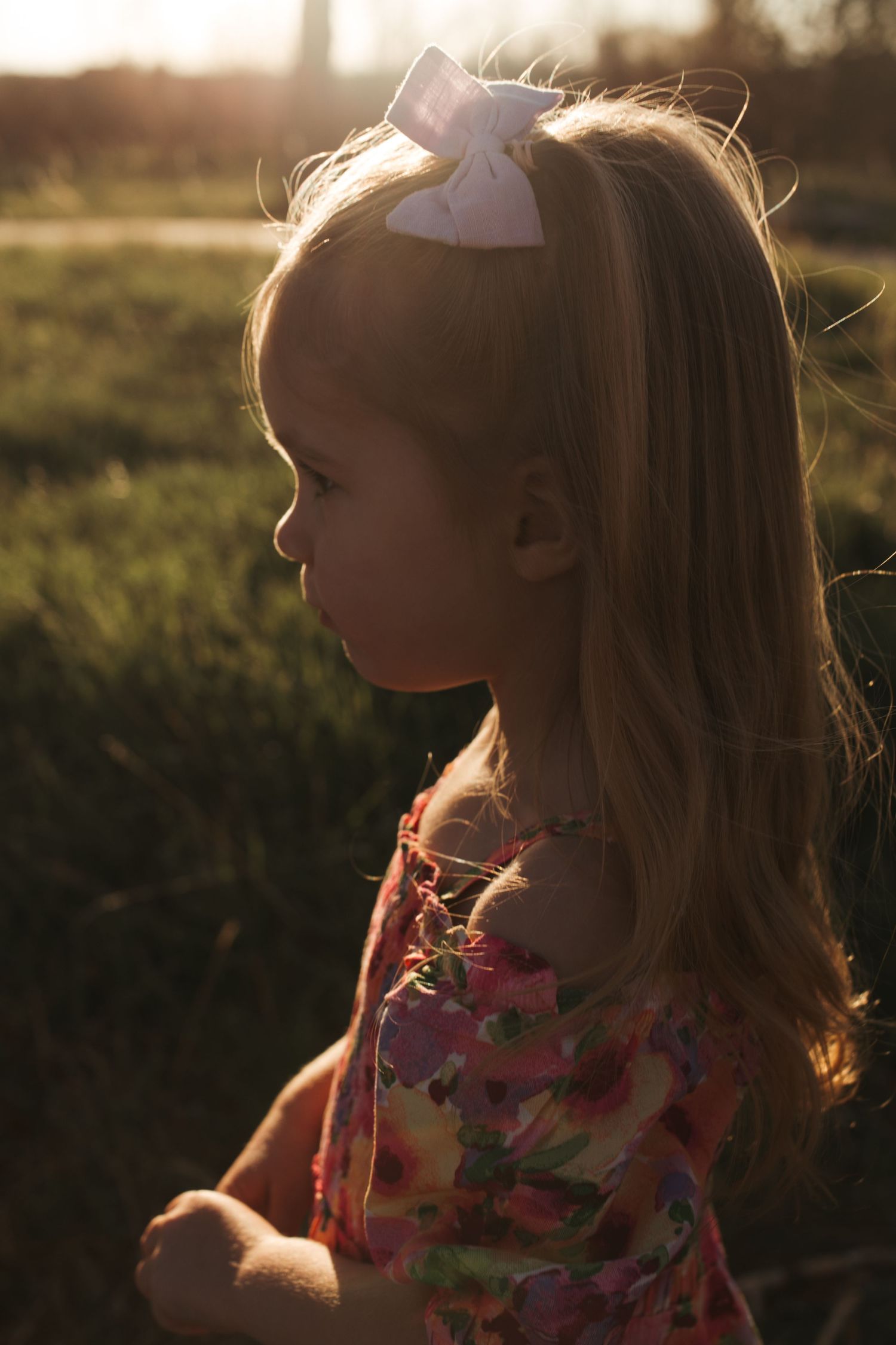 A silhouetted figure in a floral print dress gazes into golden sunlight at sunset.