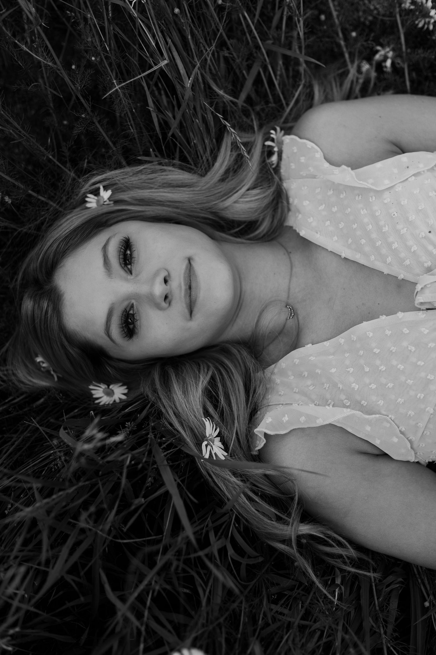 Black and white close-up portraits lying in tall grass with daisies.