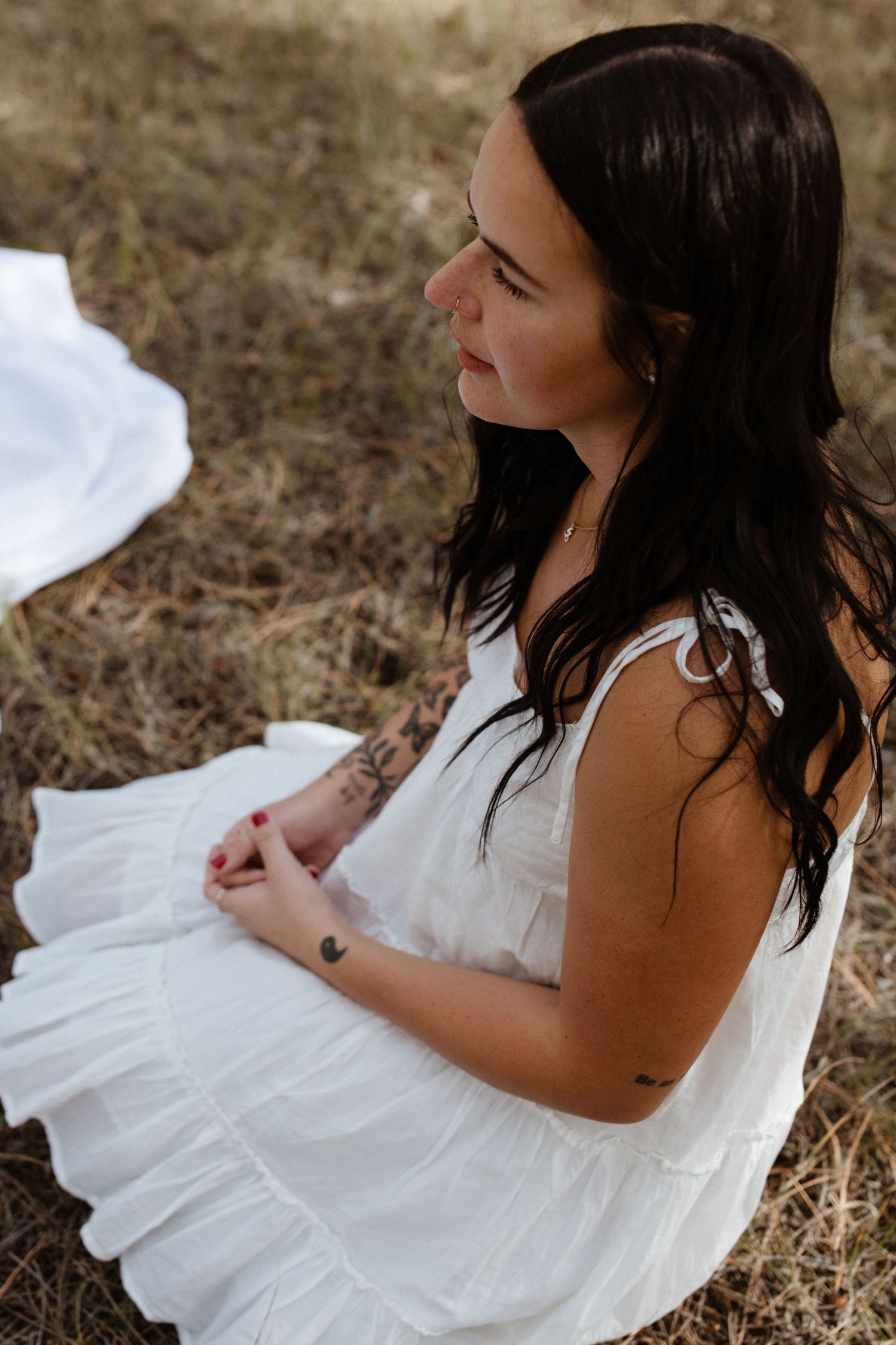 Person in white dress reclining on grass in an artistic outdoor portrait.