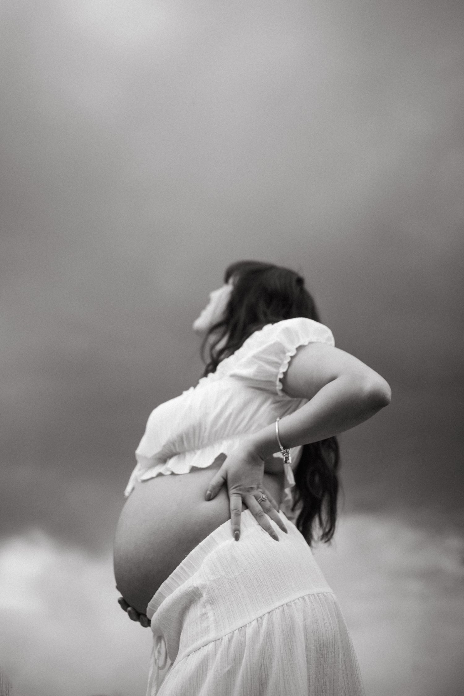 Black and white artistic photograph of a pregnant woman in a white dress shown in a series of graceful poses.