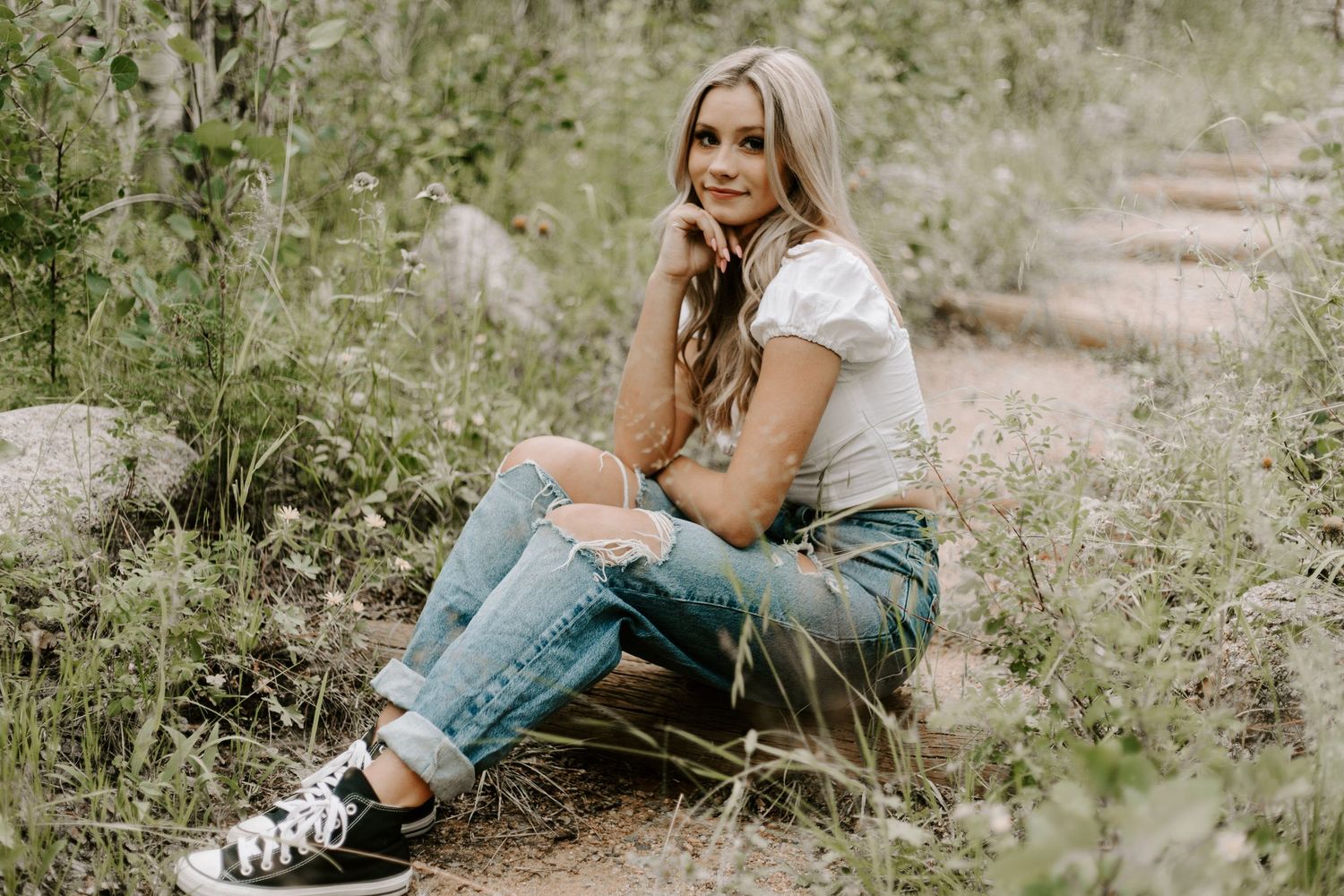 Casual outdoor portrait on dirt path wearing ripped jeans and white top with natural surroundings.
