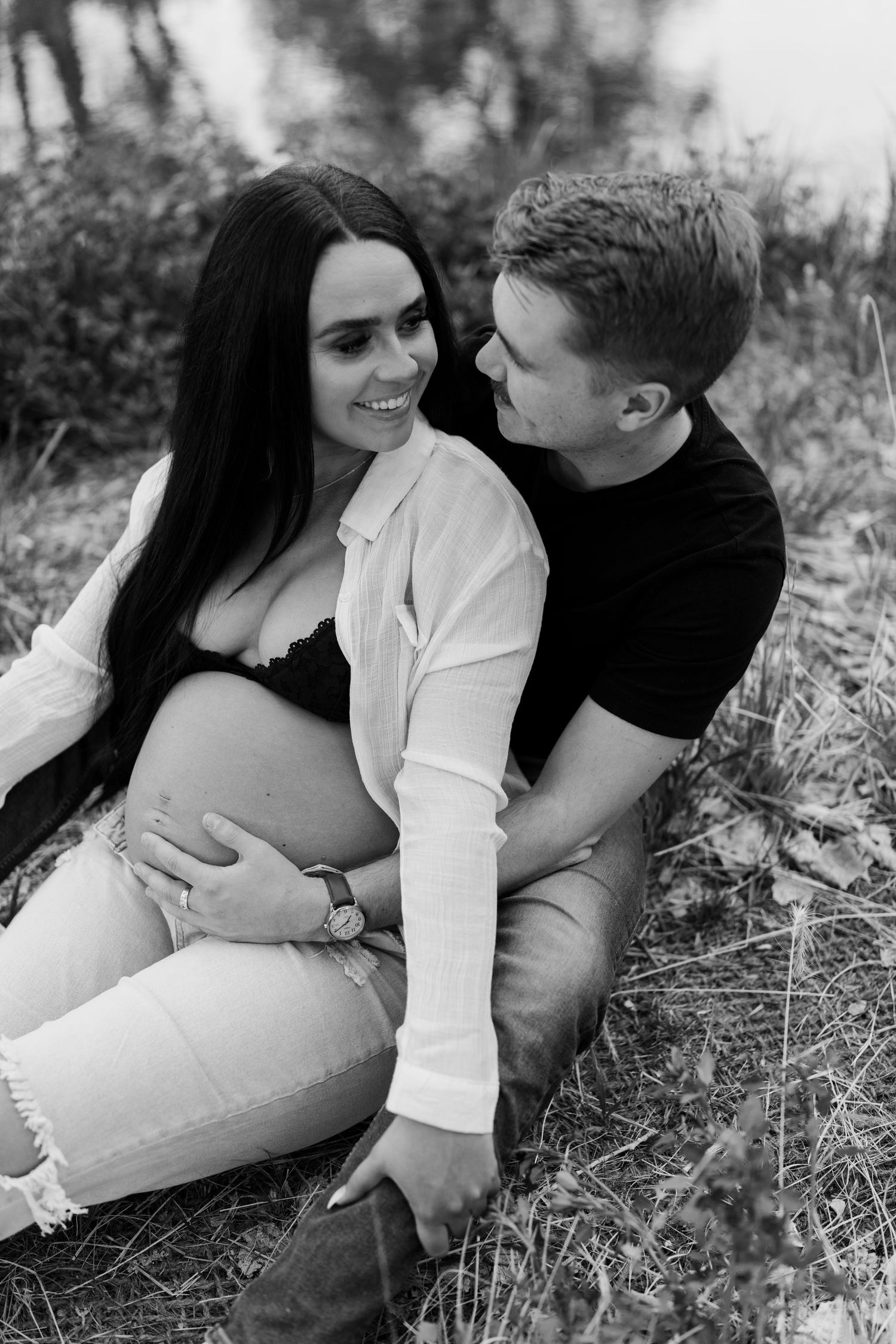 Black and white intimate maternity portrait of couple sitting in grassy field.