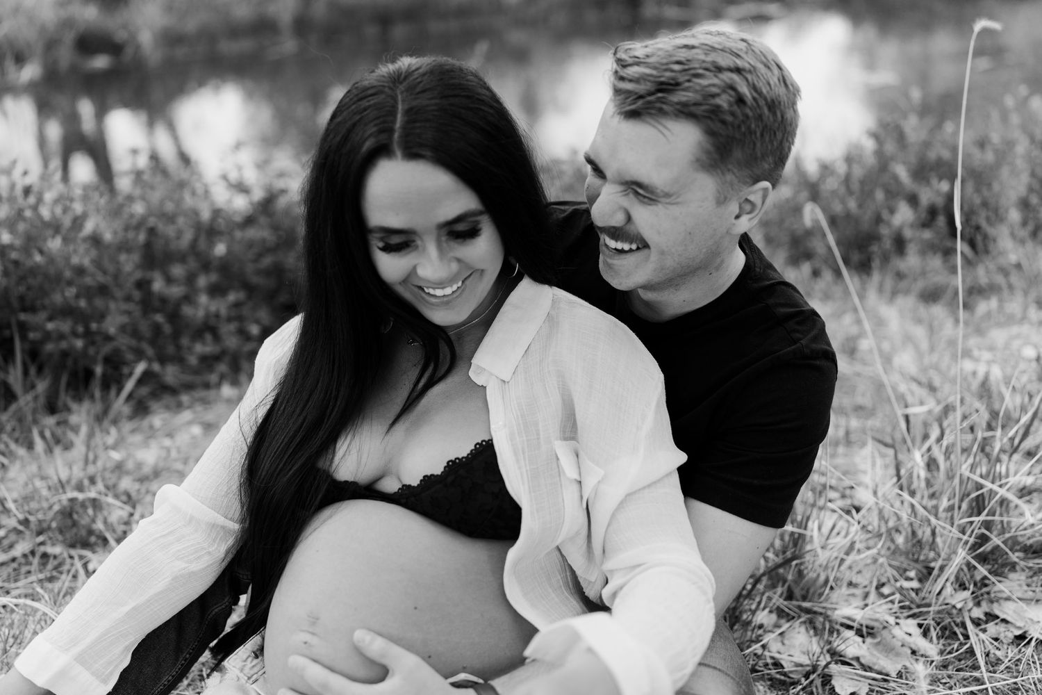 A maternity photo showing an expectant couple sharing a tender moment by a lake.