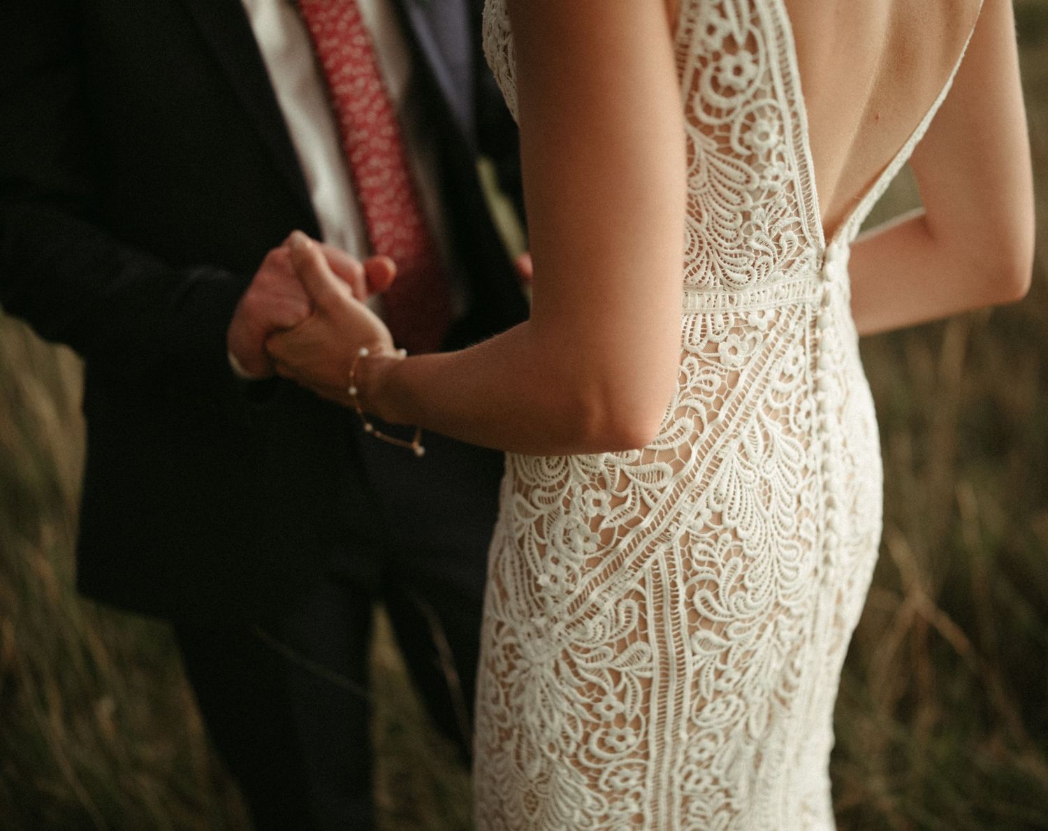 Detail shot of intricate lace pattern on white wedding dress in natural lighting.
