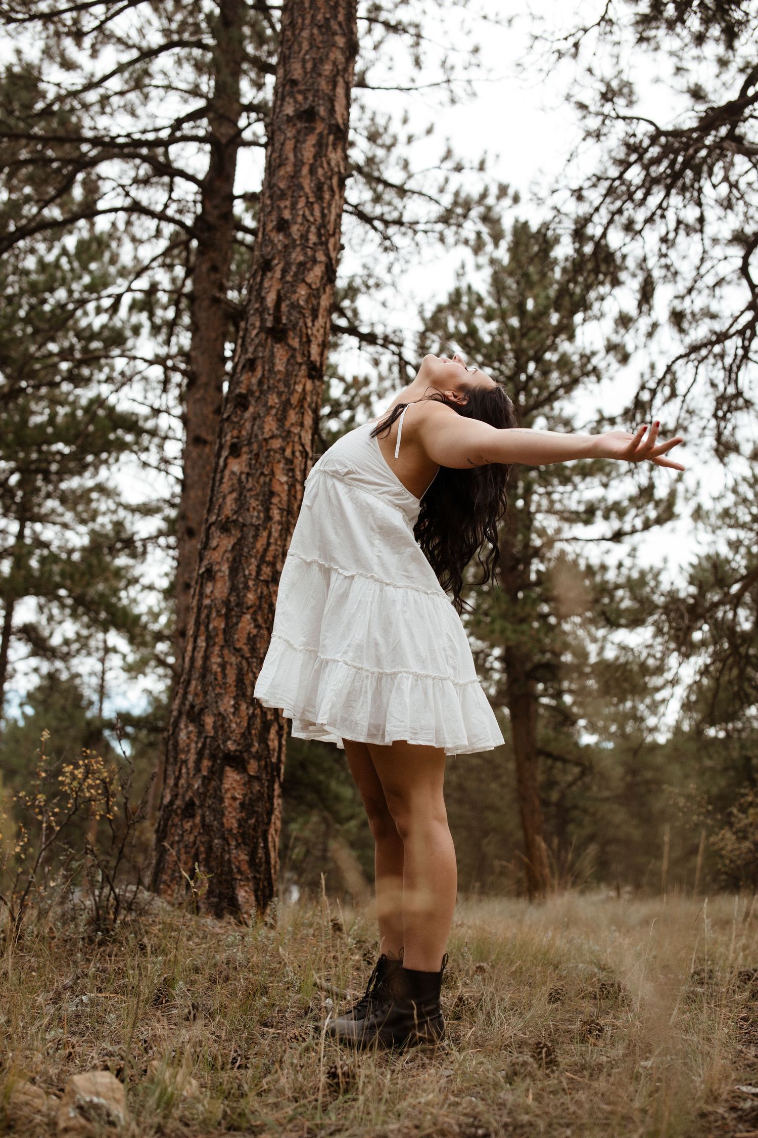 White dress flowing in motion against pine trees in a rustic outdoor setting.