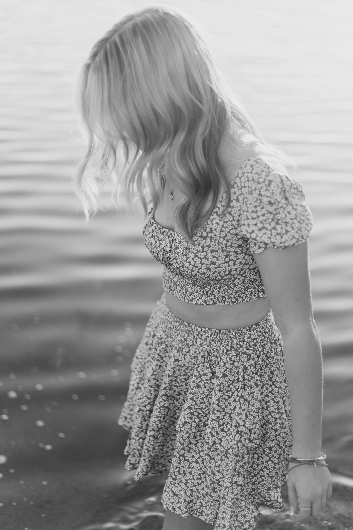 Black and white photo of person in floral dress playing by the water's edge.