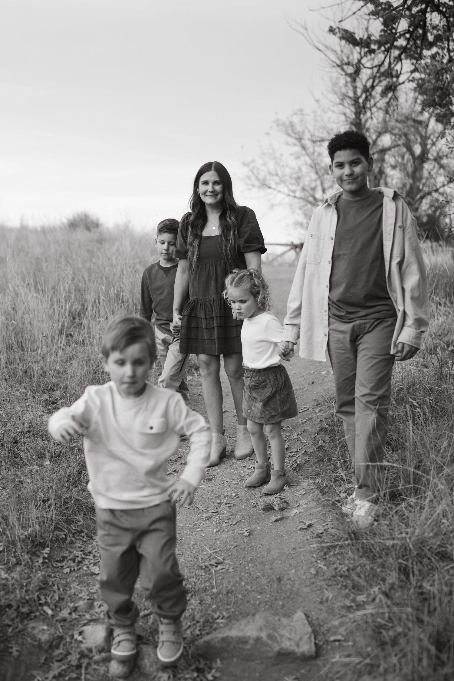 Family walking together on a dirt trail through tall grass in black and white.