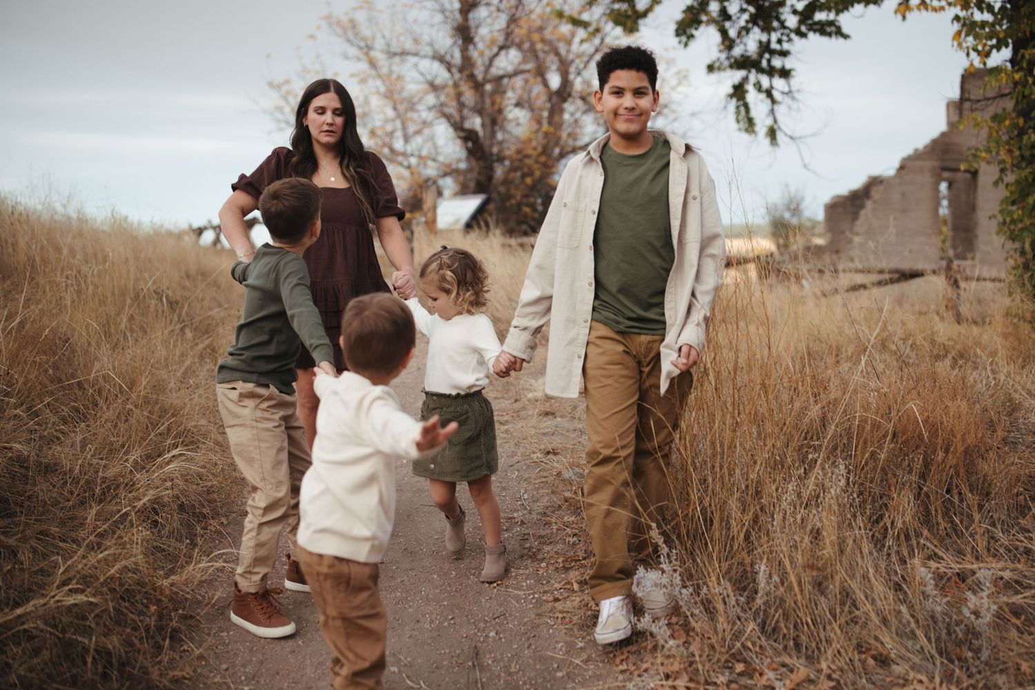 Family walking together through autumn fields at sunset during golden hour photoshoot.