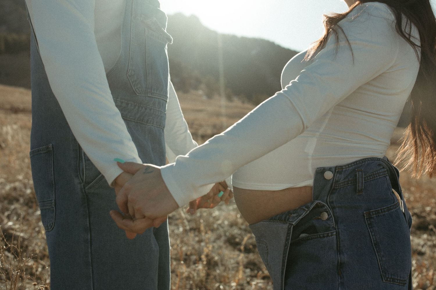 Couple embracing in a golden field with mountains in the background during sunset.