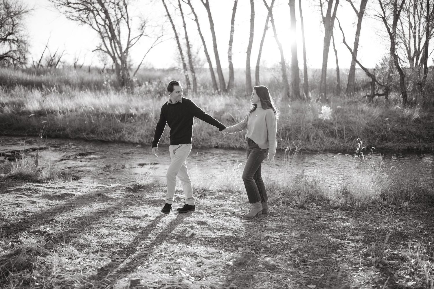 Playful couple holding hands and dancing in a winter forest clearing.